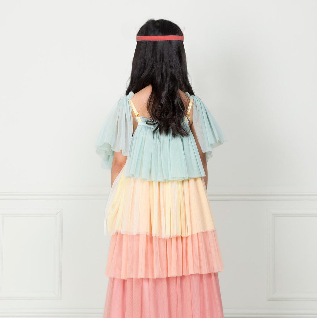 The back view of a child wearing the children’s pastel Rainbow Ruffle Princess Costume Set featuring a rainbow tulle dress with large flutter sleeves and showing the dark pink elastic band of the gold glitter crown from Meri Meri. 
