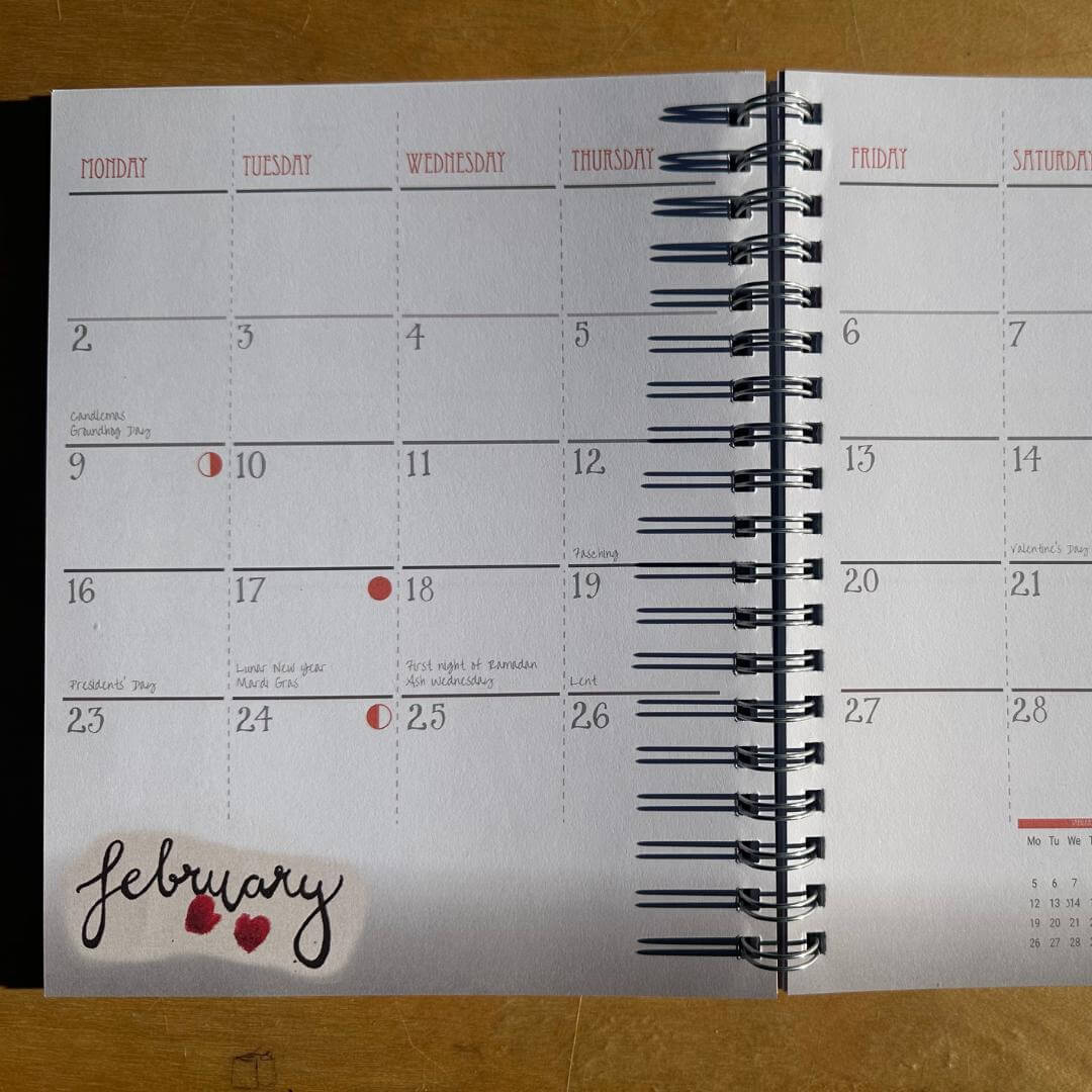 Calendar open to February with a decorative sticker on a wooden surface
