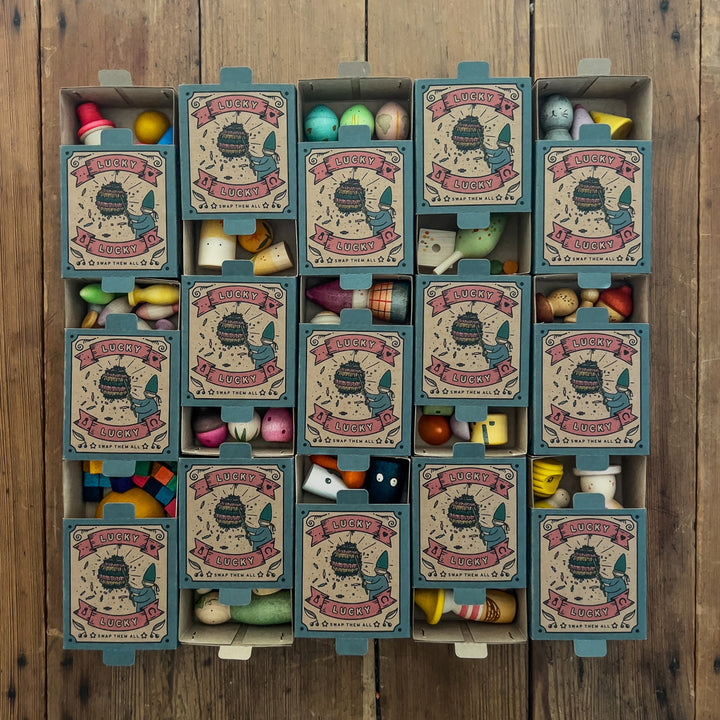 Grapat Lucky Lucky 5th Edition - image of the fronts of 15 of the boxes slide open to reveal the wooden parts inside against a wooden background - Bella Luna Toys