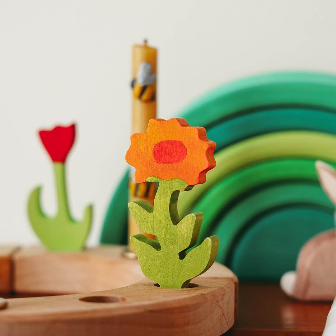 Grimm's Decorative Figure Calendula flower with a red center on a wooden base, with other toys in the background.