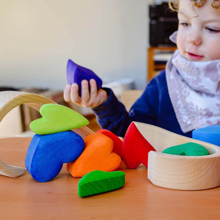 Child playing with colorful wooden shape heart toys on a table.
