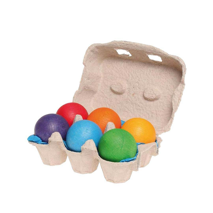 Set of colorful wooden eggs in a cardboard carton with an egg carton on a white background.