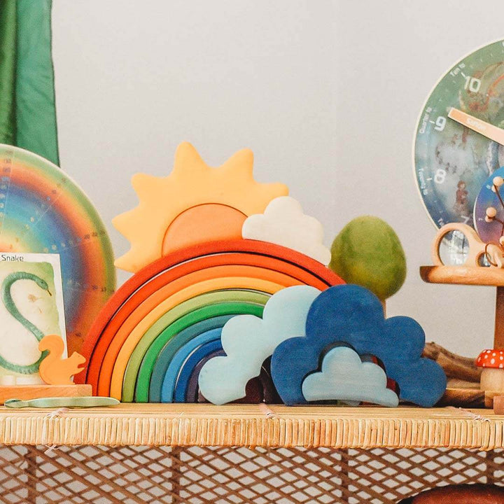 Colorful wooden toy set with rainbow, sun, and clouds on a wicker surface.