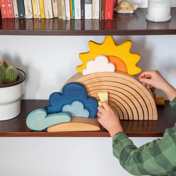 Child playing with a wooden rainbow toy on a shelf with books and plants.