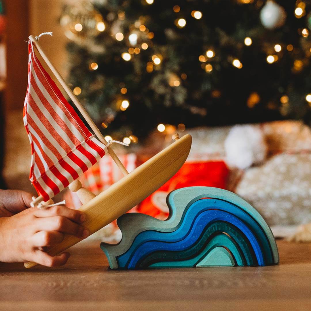 Wooden toy boat with a striped flag on blue wave shaped blocks.