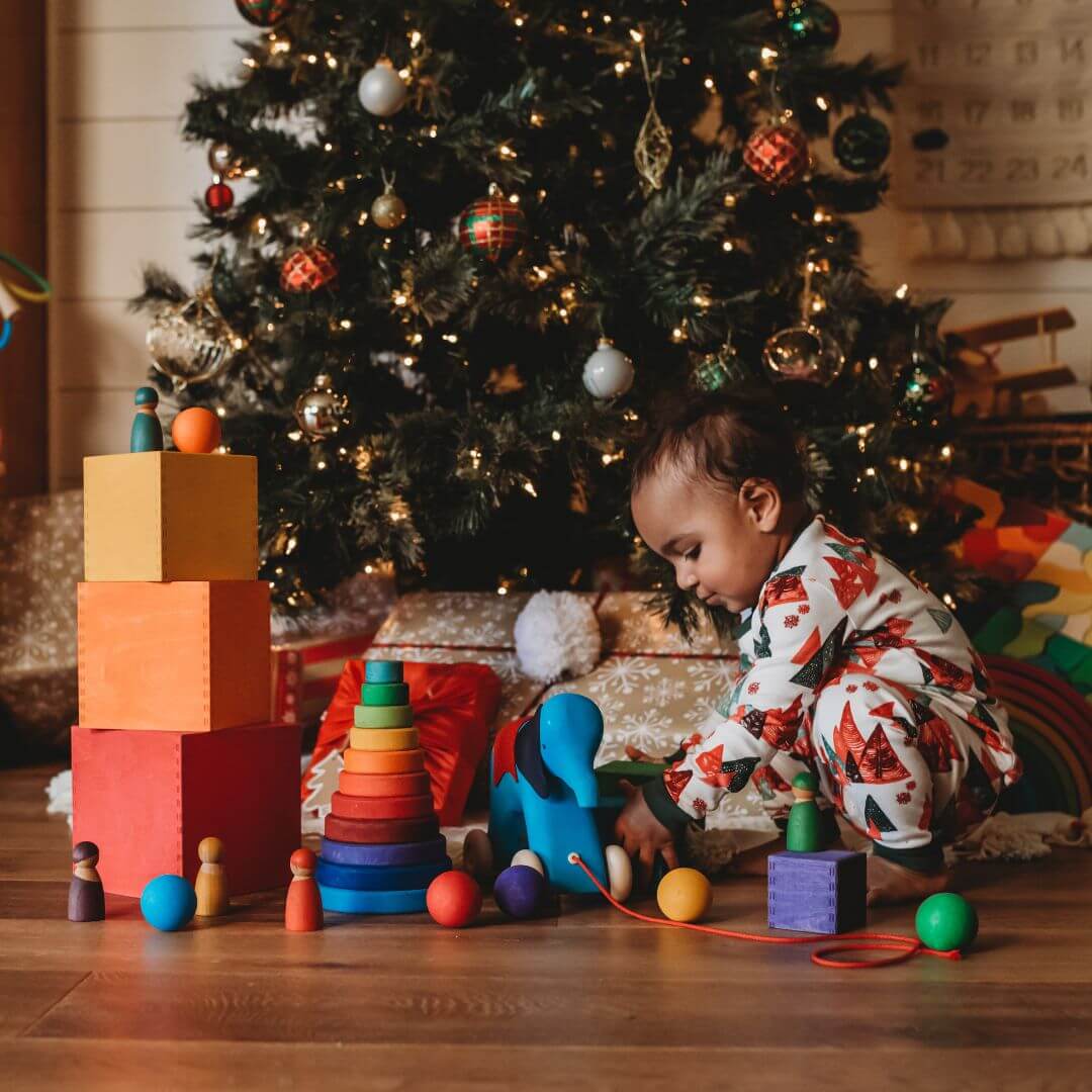 Child playing with an assortment of Grimm's wooden toys in front of a Christmas tree