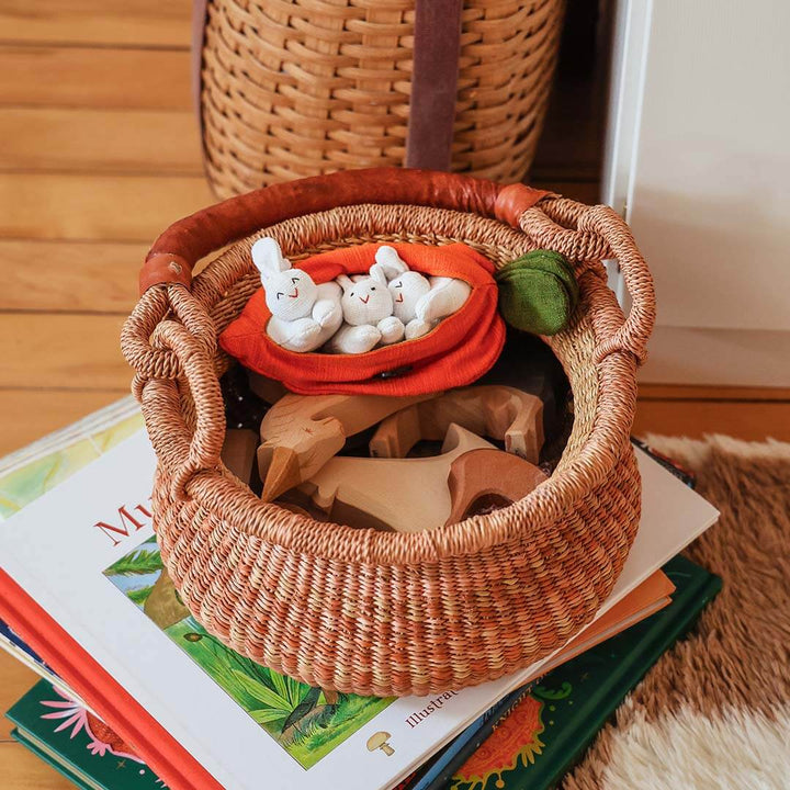 Wicker basket with toys with bunnies in a carrot on a stack of books.