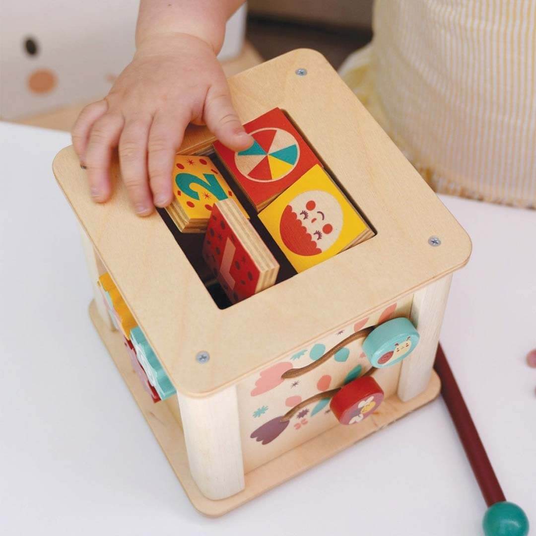 Child's hand interacting with a wooden toy block set on a white surface.