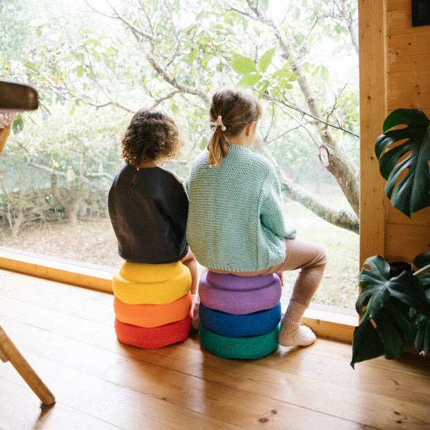 Two children sit on a stack of 3 Stapelstein steppings stones and look out a window.