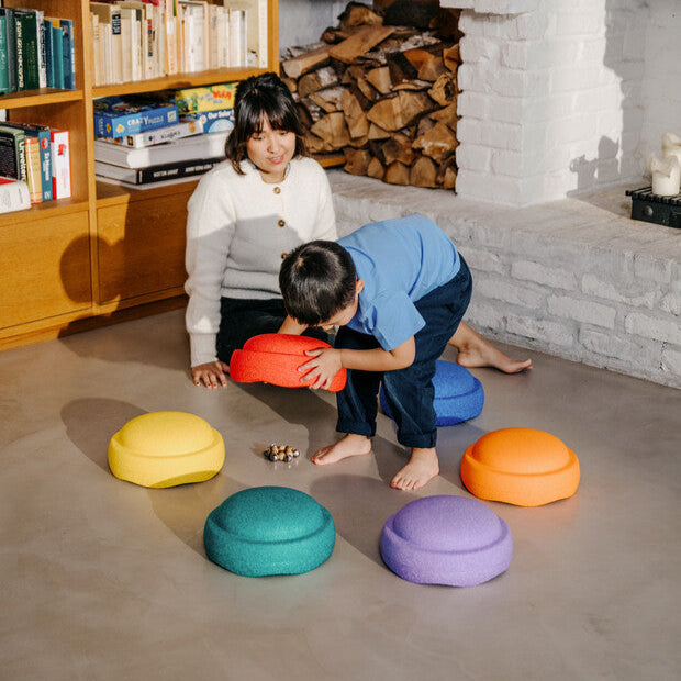 A child and parent playing a guessing game by hiding a toy under a set of rainbow Stapelstein balance and stepping stones.