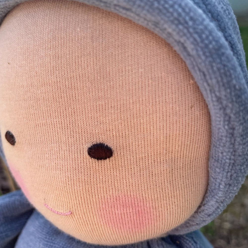 Close-up of a doll's face with a blue outfit and pink cheeks.