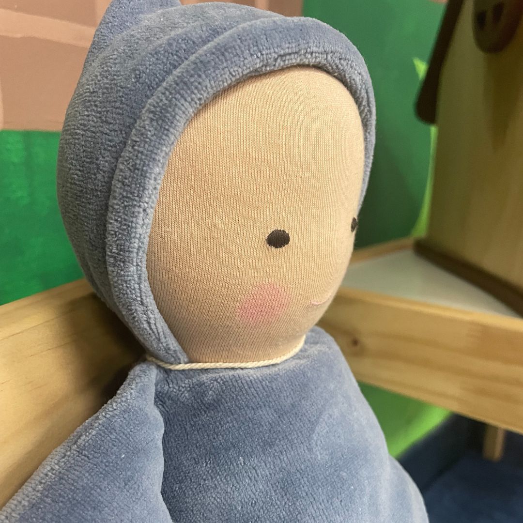Textile doll with a blue hood and face, sitting on a wooden surface.