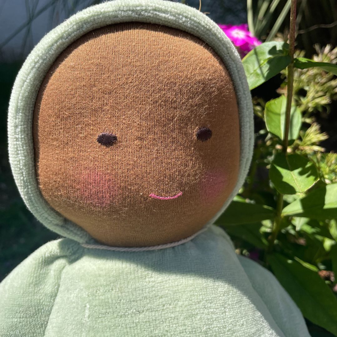 Stuffed toy with a round brown face and green clothing against a natural background