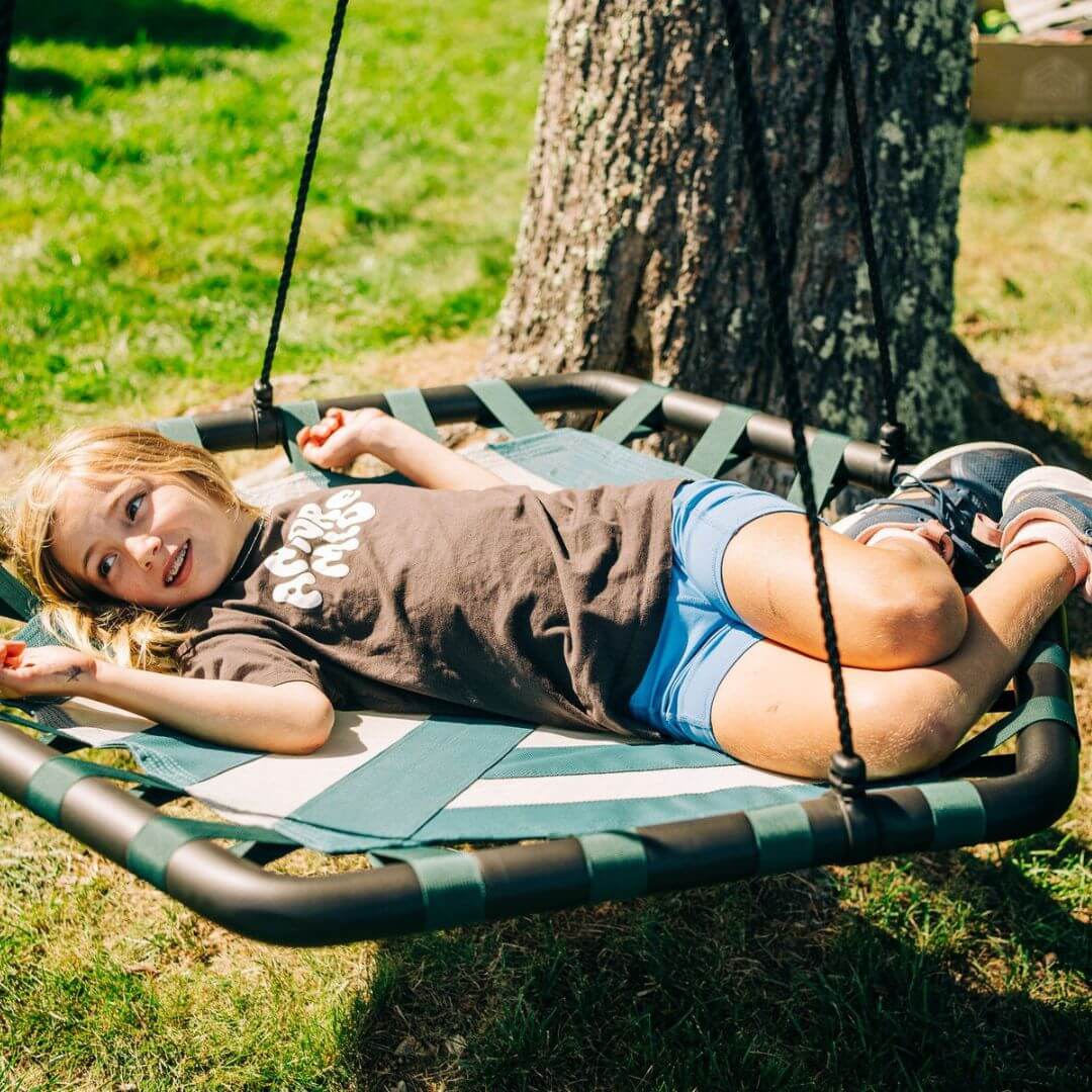 A child laying on a Bijou Build Kubix hexagon swing in the backyard.