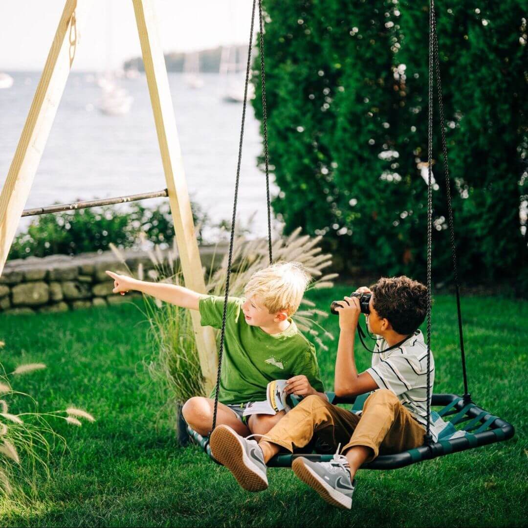 Two children sitting on a Bijou Build Kubix hexagon swing in the backyard.