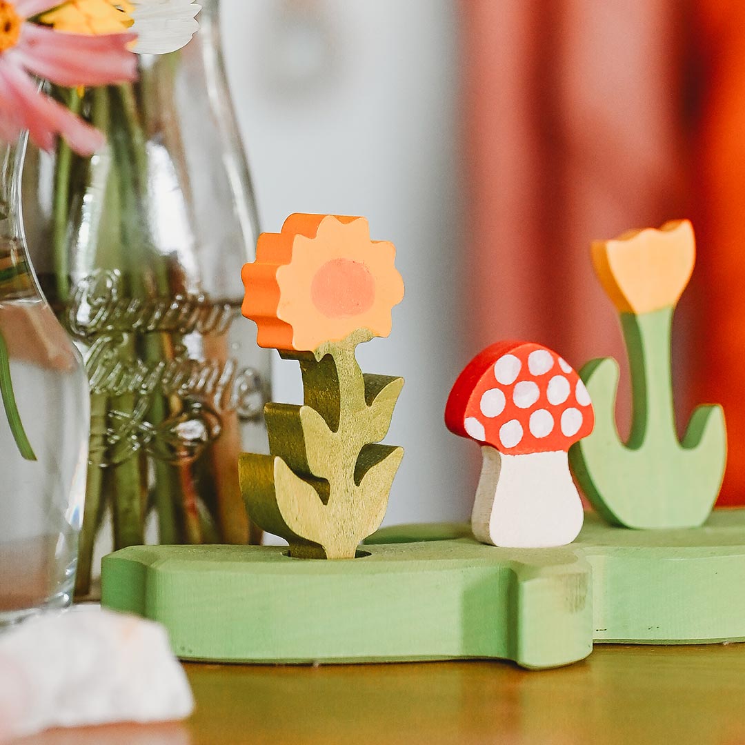 Wooden flower and mushroom toys on a green base with a blurred background.