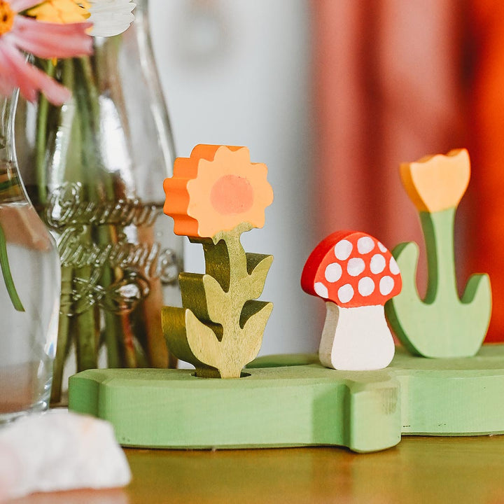 Wooden flower and mushroom toys on a green base with a blurred background.