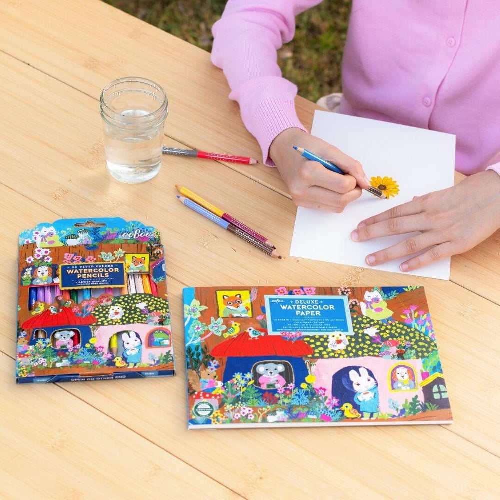 Child coloring with eeBoo watercolor pencils and paper on a wooden table
