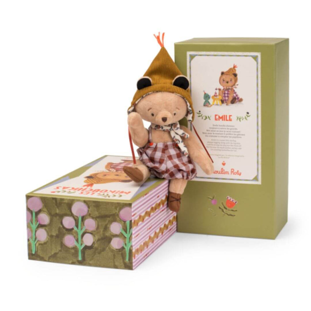 Small brown teddy bear dressed in overalls and a hat, sitting on a decorative box.