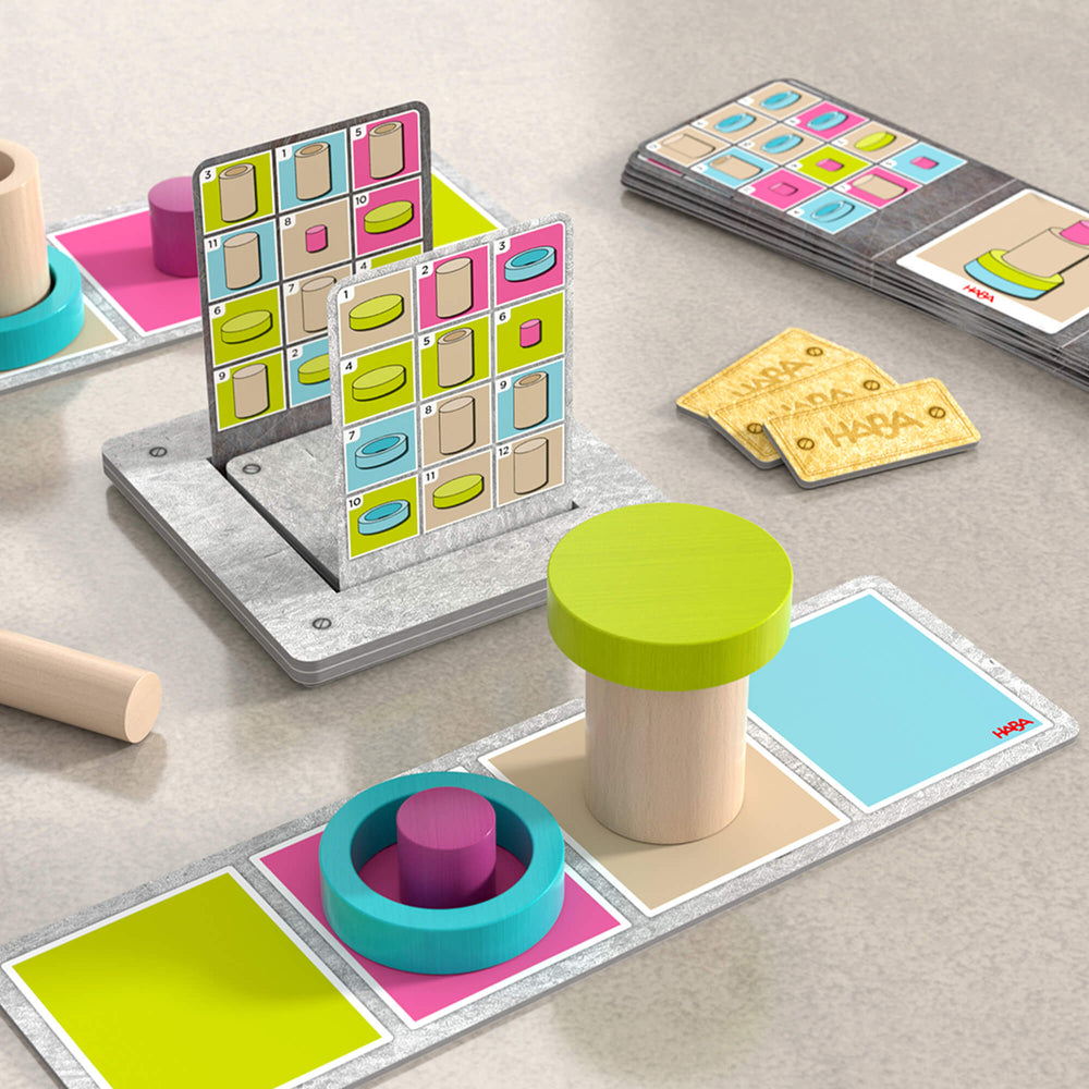 Wooden and cardboard game components show how players follow steps to move their wooden pieces through the assembly line.
