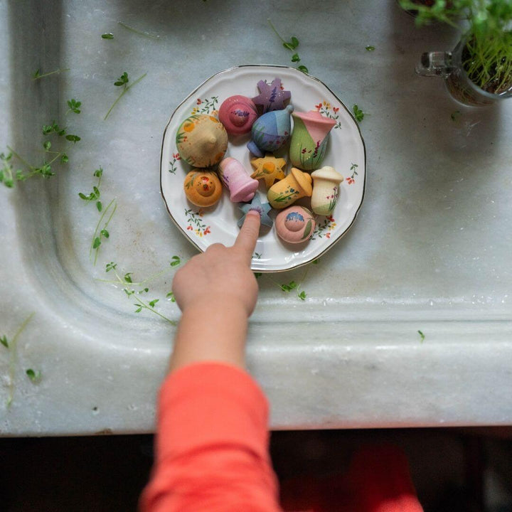 Grapat - Grapat Flower Meadow set with hand-painted wooden flower pieces in soft pastel colors, displayed on a plate with a child's hand - Bella Luna Toys