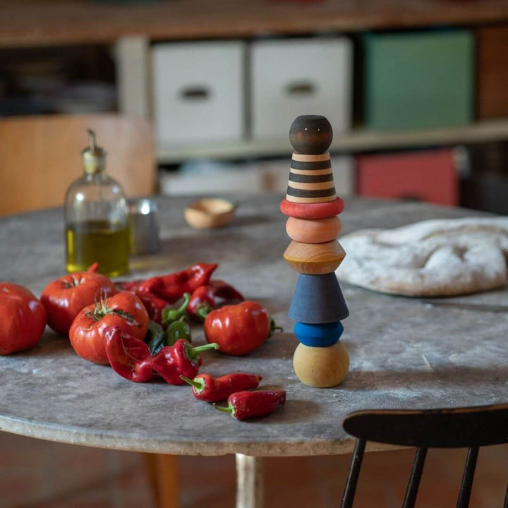 The Grapat Serendipity Stacking Tower set up in a kitchen next to tomatoes and peppers showing how  colorful and fun this handcrafted wooden toy is and what a beautiful addition it is to open-ended play.