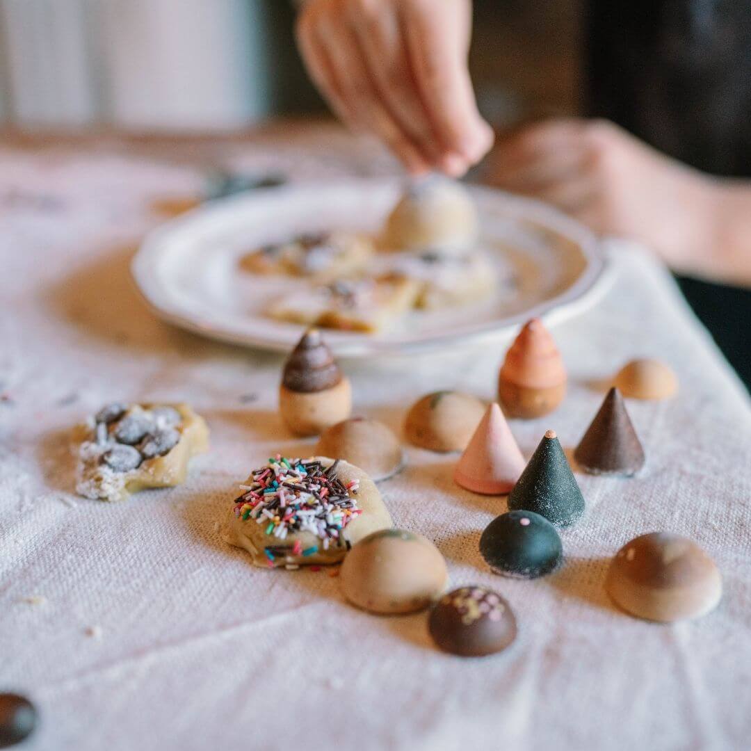 Grapat wooden breads and cookies play set with 12 hand-painted wooden bakery pieces shown on a tablecloth with real baked goods nearby - Bella Luna Toys