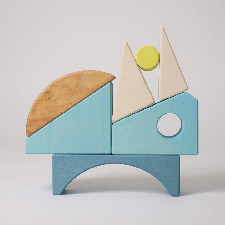 Grimm’s Wooden Puzzle and Building Set in blue shown with organic-shaped pieces arranged outside the frame, forming playful sculptures and designs.