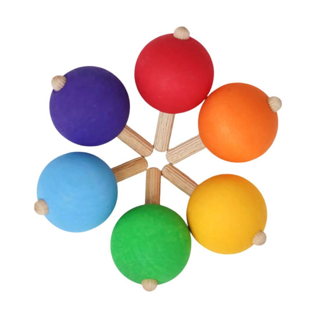 Top-down view of six colorful wooden spinning tops arranged in a rainbow circle, each with a round ball handle, crafted by Grimm’s.