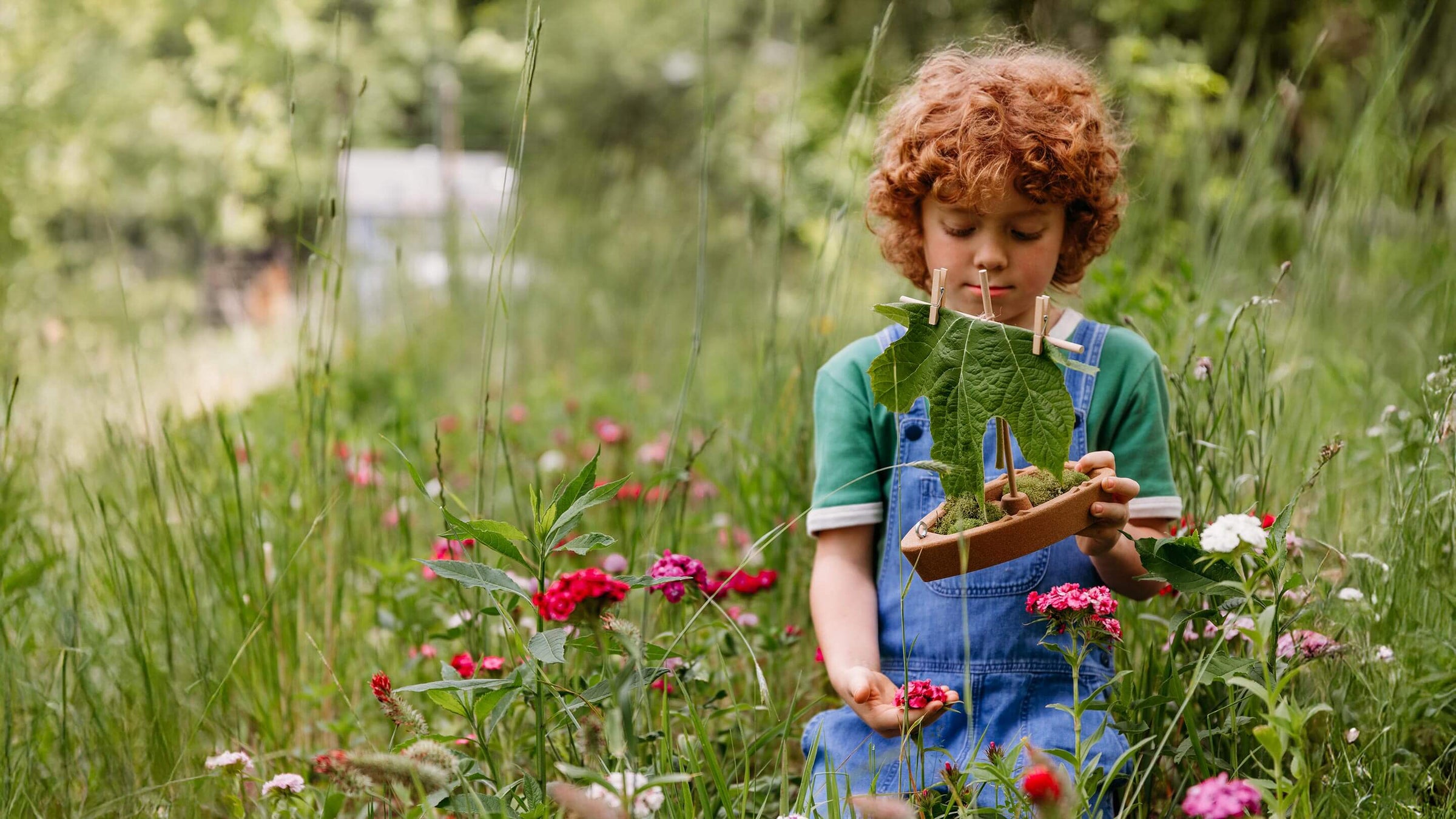 Child holding a cork boat toy with flowers and greenery.