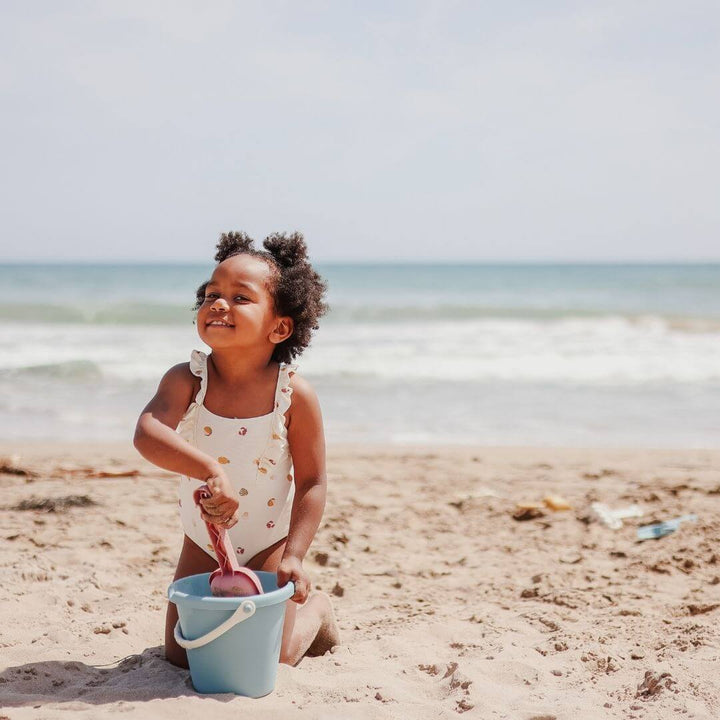 A little girl on the beach with sand toys and waves behind her. Miniland - ECO Large Sand Toys 4 Piece Set - Bella Luna Toys