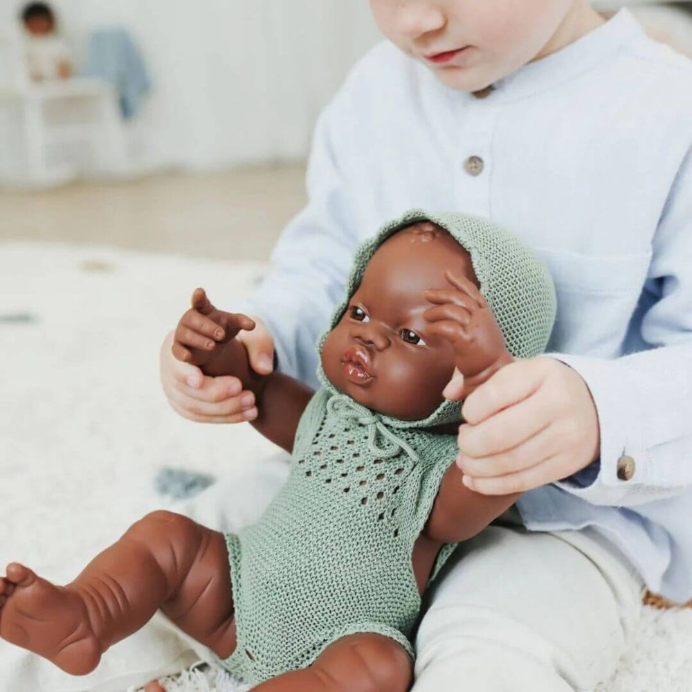 Miniland - Child playing with a Miniland realistic doll that is wearing a Miniland Knitted Doll Outfit for 15'' doll – Romper & Bonnet in a playroom setting - Bella Luna Toys