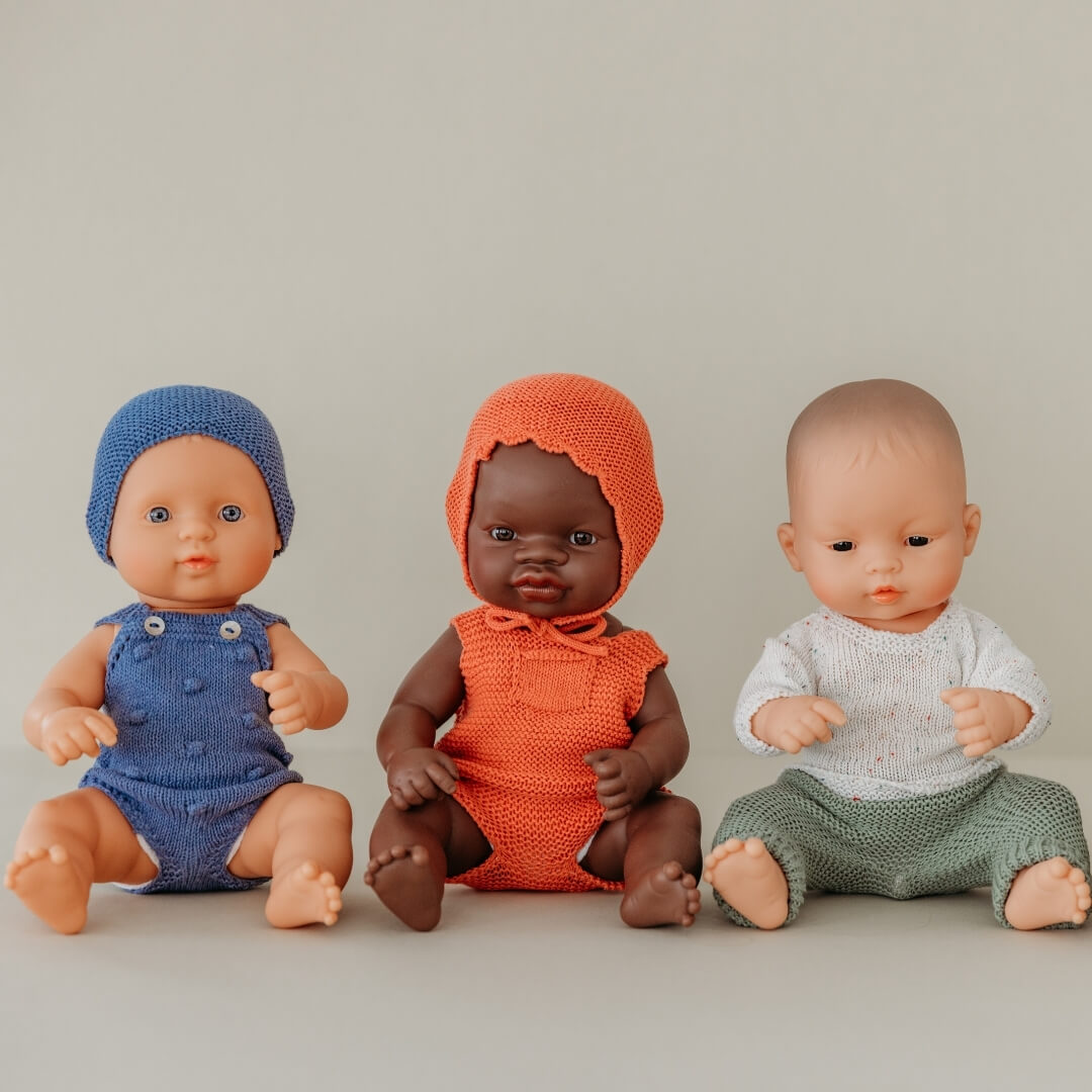 Three dolls in blue, orange, and green outfits on a neutral background