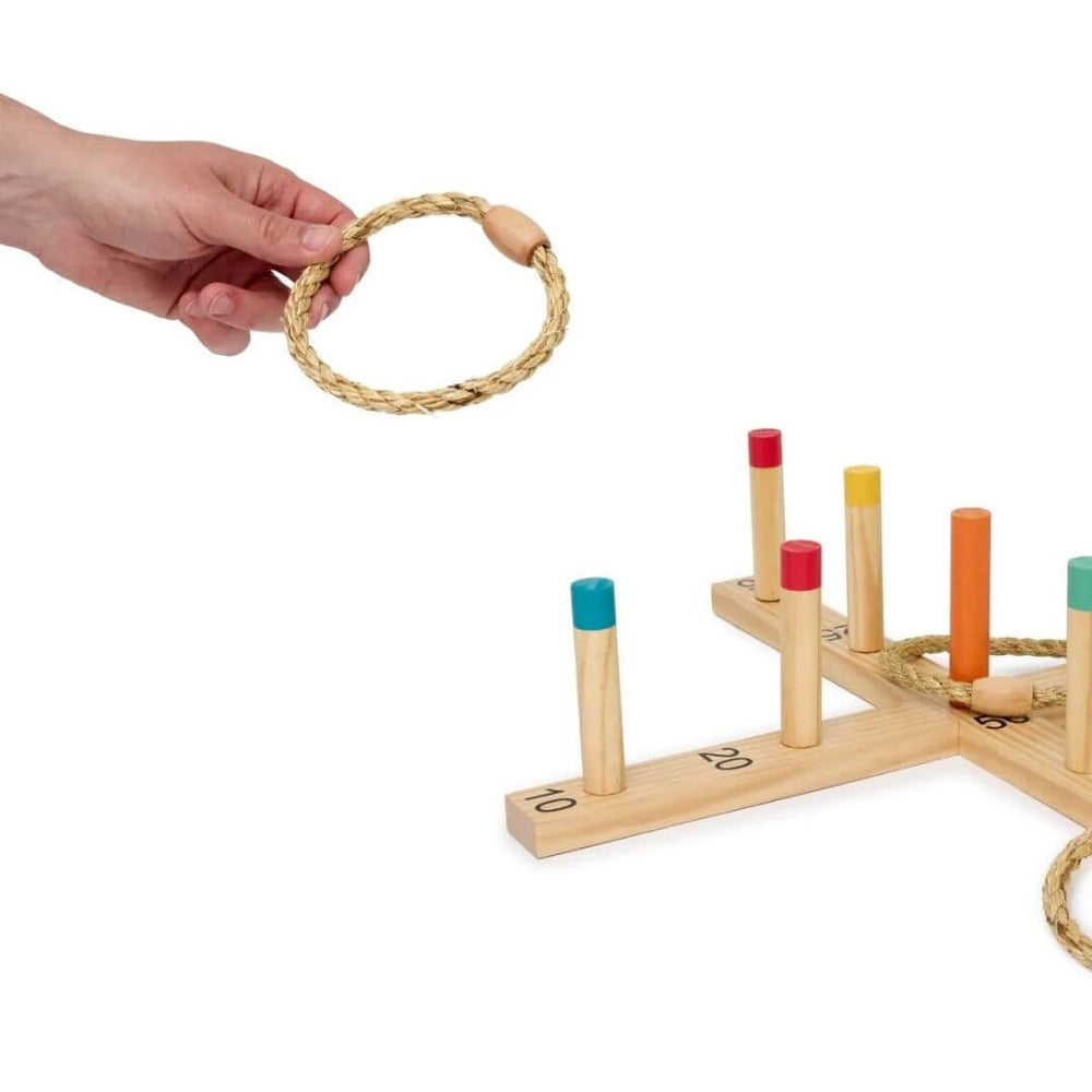 Miniland - A hand holding one of the rope rings for the wooden Miniland ring toss game featuring numbered scoring pegs, colorful target posts, and natural rope rings arranged on a cross-shaped wooden base - Bella Luna Toys