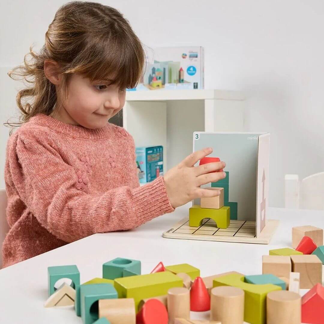 Miniland - Child plays with Shape Makers learning game with 40 colorful wooden building pieces, 24 challenge cards, and 4 player boards in a playroom setting - Bella Luna Toys