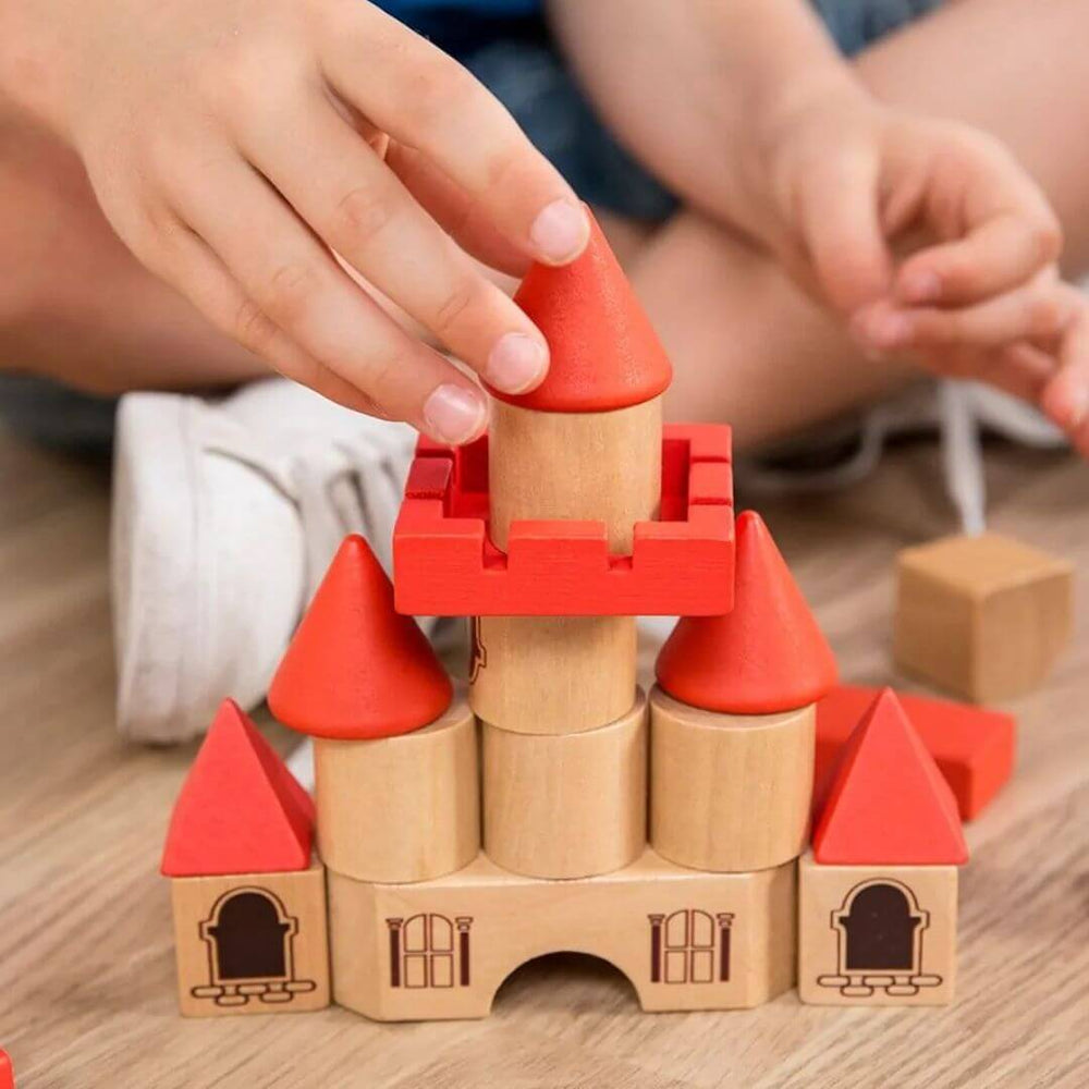 Miniland - Child playing with wooden castle building block set made from sustainable wood, featuring natural and red architectural blocks arranged into a large castle with towers, arches, staircases, and turrets on the floor - Bella Luna Toys