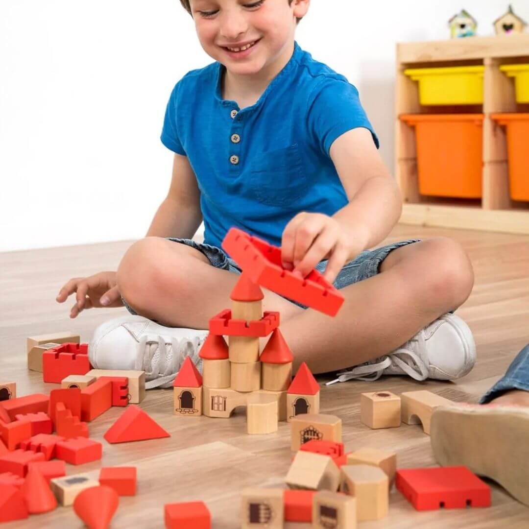 Miniland - A child in a playroom playing with wooden castle building block set sitting cross-legged on the floor - Bella Luna Toys