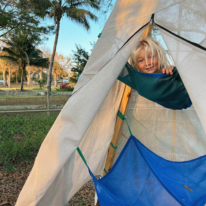 Child peeking out from a tent with palm trees and a clear sky in the background