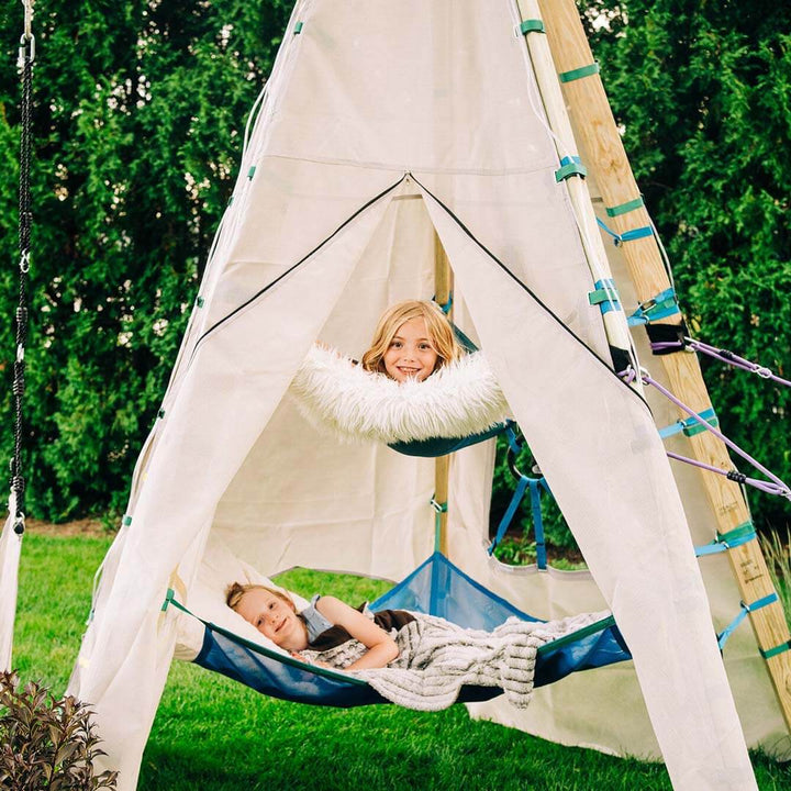 A children's teepee-style play tent with two kids resting in blue hammocks inside, set on green grass with a hedge background.