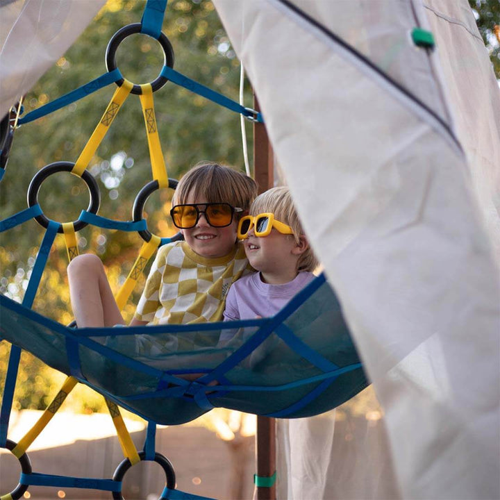 Two children wearing sunglasses on a playground structure with a blurred natural background