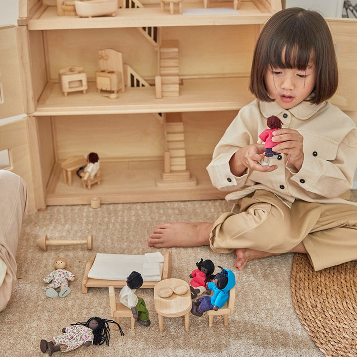 Child interacting with a miniature wooden dining set inside a dollhouse, enhancing storytelling play.