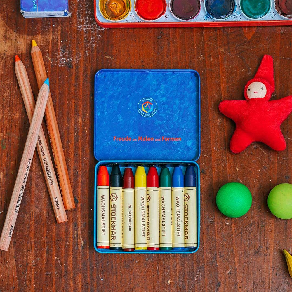 Colorful crayons in a tin on a wooden surface with art supplies.