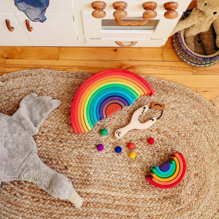 Colorful wooden rainbow toys on a woven mat with a wooden cabinet in the background.