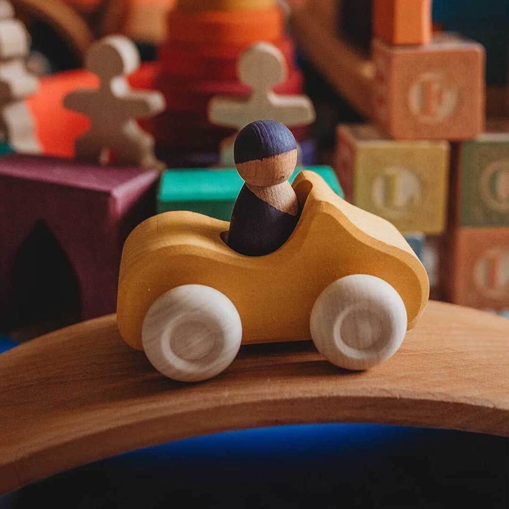 Wooden toy car with a driver figure on a wooden track, surrounded by colorful blocks and toys.