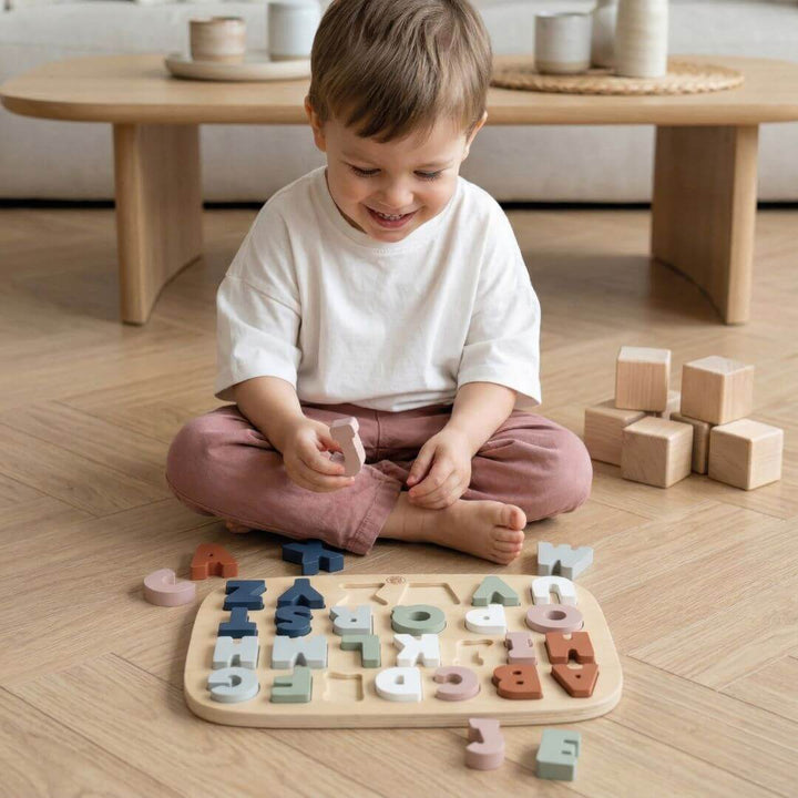 Child playing with Speedy Monkey wooden alphabet puzzle with chunky pastel-coloured letters on a wooden surface with a few of the letters out of the puzzle frame - Bella Luna Toys 