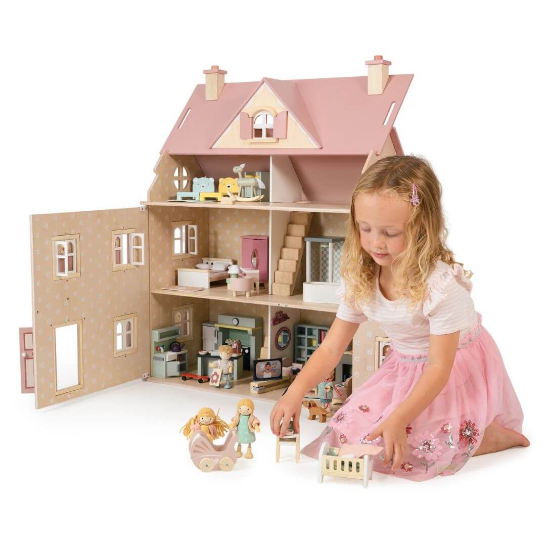 Tender Leaf - Alouette House with a slight side angle against a white background. A child in the foreground is playing with the furniture and figures that pair with the house. - Bella Luna Toys