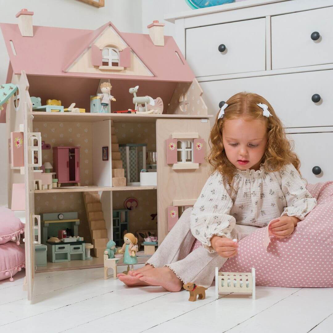 A child sitting next to the Allouette Dollhouse, playing with a small wooden figure from Tender Leaf Toys.