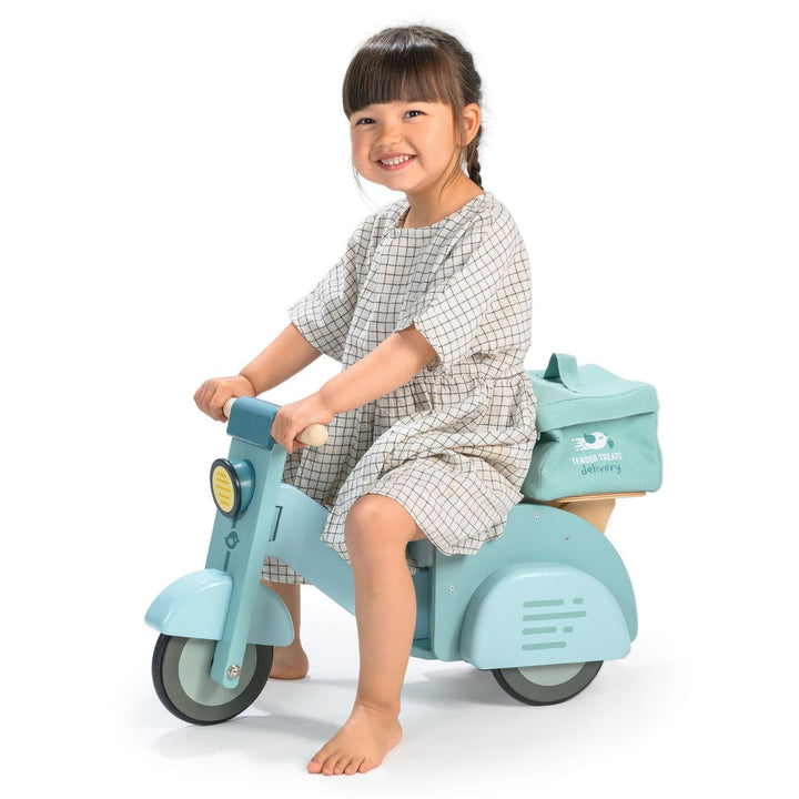 Child sitting on Tender Leaf Toys delivery scooter with a white background.