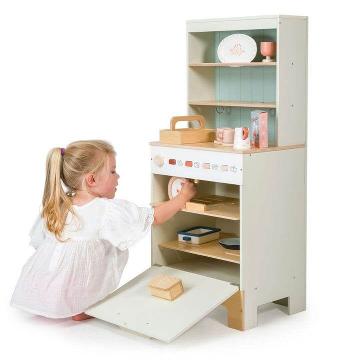 A child is loading dishes into the wooden dishwasher from Tender Leaf Toys.