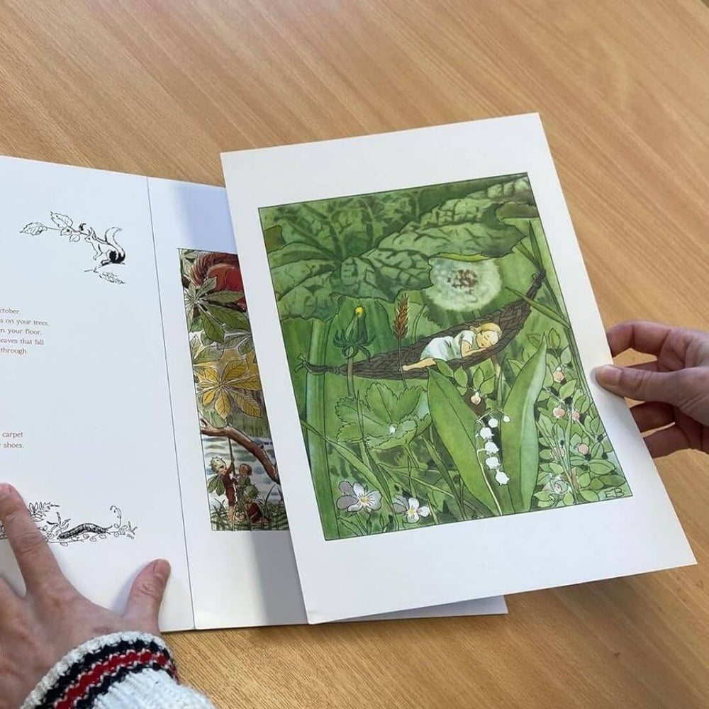 Hands holding an open book, revealing a removable illustrated print of a lush green forest scene from The Art of Elsa Beskow, with intricate botanical details.